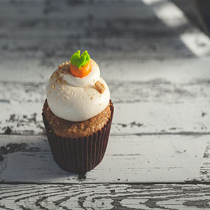 A carrot cake flavored cupcake with cinnamon accents and a cream cheese frosting.