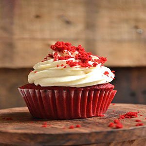 A red velvet cupcake with a deep rich red color and cream cheese frosting on top.